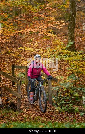 Nette Seniorin, die ihr E-Mountainbike auf den herbstlichen Waldwegen in der Nähe von Stuttgart, Baden-Württemberg, fährt Stockfoto