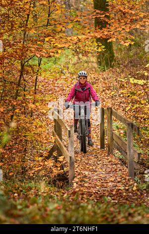 Nette Seniorin, die ihr E-Mountainbike auf den herbstlichen Waldwegen in der Nähe von Stuttgart, Baden-Württemberg, fährt Stockfoto