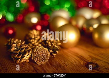 Weihnachtliches Stillleben mit goldenen Tannenzapfen und Kugeln und Lametta auf Holztisch und goldenem Licht Stockfoto