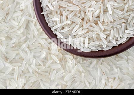 Weißer länglicher Basmati-Reis in einer braunen Tonschale vor einem Hintergrund von Streureis. Draufsicht mit Kopierbereich. Stockfoto