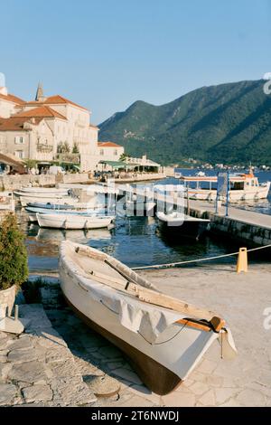 Das Fischerboot in einer Decke liegt am Ufer in der Nähe eines Piers mit verankerten Booten. Perast, Montenegro Stockfoto