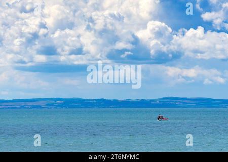 Ein kleines Fischerboot an der Küste, das vor der Ostküste Schottlands seine Krabbentöpfe oder -Kreaturen pflegt und von den großen Sommernäulen der Cumulo-nimbus-Wolken im Schatten steht. Stockfoto