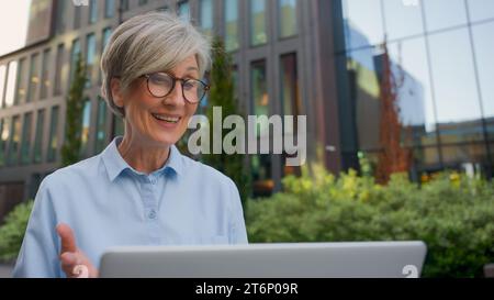 Kaukasische Erwachsene 50er-Frau lächelnd reife Geschäftsfrau Arbeitgeber Geschäftsfrau plaudert im Freien mit Kunden Online-Computervideo Stockfoto