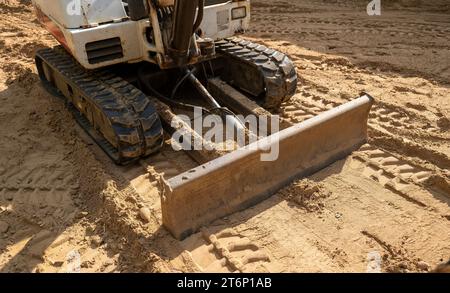 Ein Minibagger, der auf braunem Boden geparkt ist, mit Nahaufnahme des Schilds und der Ketten auf einer neuen Baustelle. Stockfoto