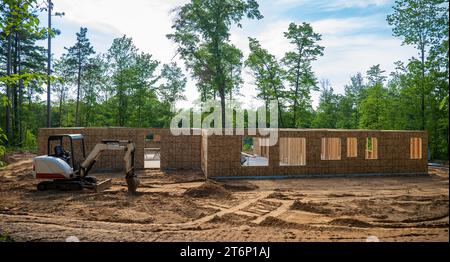 Neues Wohnbauprojekt auf einem bewaldeten Baugrundstück mit einem Minibagger, der auf dem Boden auf der Baustelle geparkt ist. Stockfoto