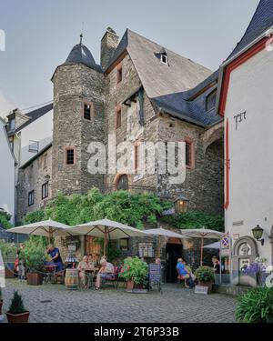 Geschäftiges Café im Freien auf dem Altstadtplatz im mittelalterlichen Beilstein, Moselregion, Deutschland, mit alten Steinbauten im Hintergrund. Stockfoto