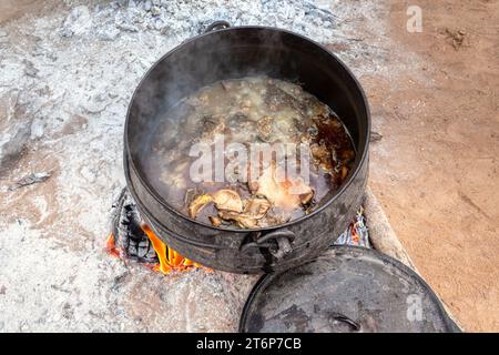 afrikanischer Topf draußen in der Hofküche, der große Stücke Fleisch Kutte und Fett kocht Stockfoto