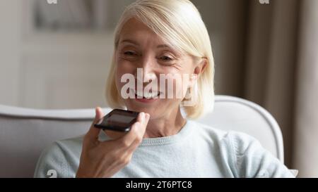 Lächelnde, reife Frau, die ein Smartphone hält und Sprachnachrichten aufnimmt Stockfoto