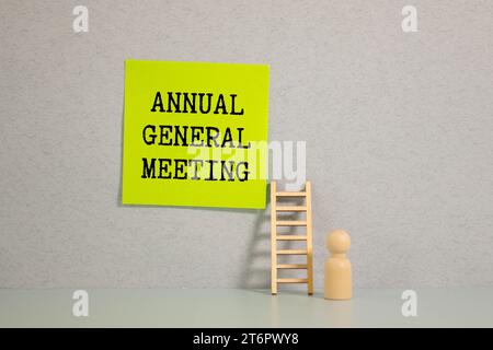 AGM Annual General Meeting ist in Rot auf einem weißen Blatt Papier auf hellgelbem Hintergrund neben einem Laptop, Stift, einer Lupe, einer Brille A geschrieben Stockfoto