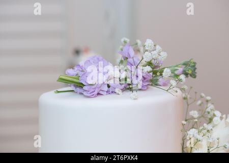 Weiße Hochzeitstorte mit lila Blumenschmuck aus nächster Nähe Stockfoto