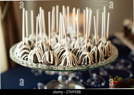Schokoladenlollypops mit weißen Vanillestreifen, alle auf runden Silberteller am Hochzeitsempfang Desserttisch aufgereiht Stockfoto
