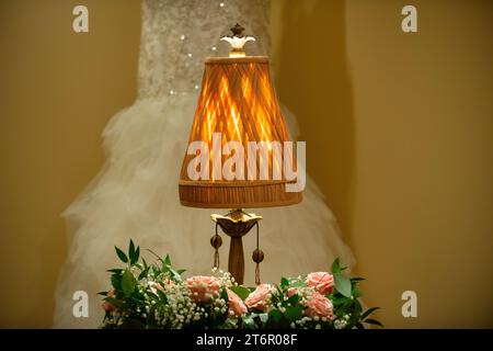 Warme antike Lampe auf dem Tisch mit Rosen und Hochzeitskleid im Hintergrund Braut bereit Stockfoto