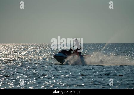 Silhouette eines schnell fahrenden Mannes auf Jetski auf glitzerndem Meer. Klares Meer und blauer Himmel, Nahaufnahme Stockfoto