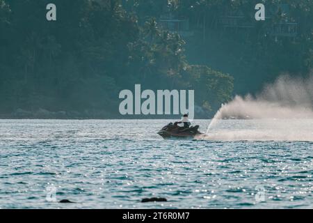 Schnell fahrende schwarze Frau auf Jetski auf glitzerndem Meer. Verschwommener tropischer Wald, Nahaufnahme Stockfoto