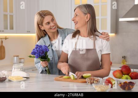 Tochter mit schönen Kornblumen besucht ihre reife Mutter zu Hause Stockfoto