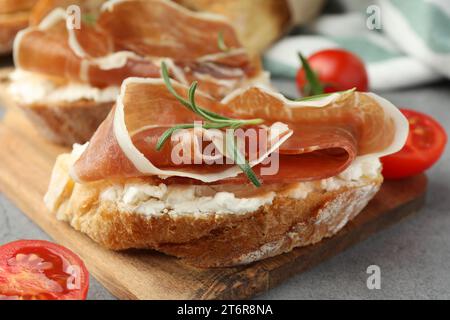 Leckere Sandwiches mit geräuchertem Schinken, Tomaten und Rosmarin auf grauem Tisch, Nahaufnahme Stockfoto