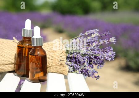 Flaschen mit ätherischem Öl und Lavendelblüten auf weißer Holzoberfläche im Freien, Platz für Text Stockfoto