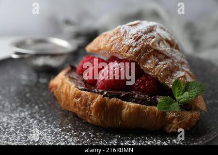 Köstliches Croissant mit Himbeeren, Schokolade und Puderzucker auf Teller, Nahaufnahme Stockfoto