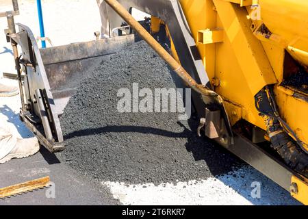 Als Teil des Straßenbaues wird Asphalt auf oberem Schotterboden mit frischem Bitumenasphalt verlegt Stockfoto