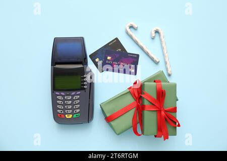 Zahlungsterminal mit Kreditkarten, Weihnachtsgeschenkboxen und Bonbons auf blauem Hintergrund Stockfoto