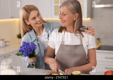 Tochter mit schönen Kornblumen besucht ihre reife Mutter zu Hause Stockfoto