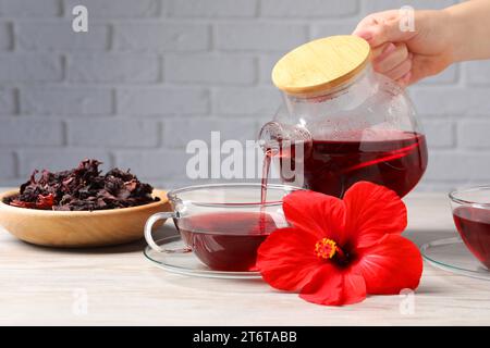 Frau, die leckeren Hibiskus-Tee in eine Tasse an einem hellen Holztisch gießt, Nahaufnahme Stockfoto