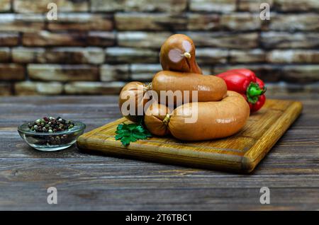 Klassische gekochte Würstchen auf einem Schneidebrett mit Pfeffer, Petersilie auf einem Holztisch. Hintergrund aus dekorativem Stein Stockfoto