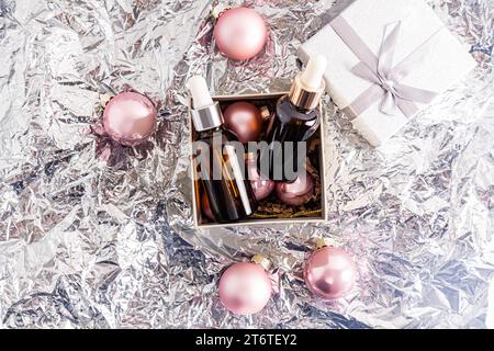 Zwei Kosmetikflaschen mit einer dunklen Glaspipette mit einem natürlichen Selbstpflegeprodukt in einer offenen Silvesterbox. Geschenkkonzept. Silberner Hintergrund Stockfoto