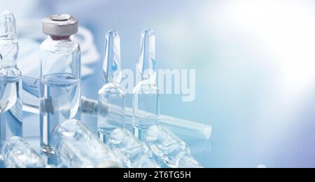 Eine Arzneimittelampulle, eine medizinische Spritze und Einwegmasken sind Nahaufnahme auf einem hellblauen Hintergrund. Stockfoto