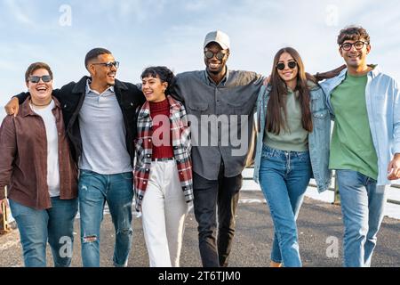 Gruppe junger, vielfältiger Freunde, die gemeinsam spazieren und lachen, um Einheit und Glück zu zeigen. Stockfoto