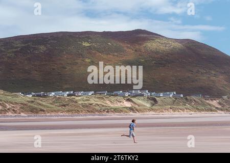 Ein Junge läuft gerne am riesigen Sandstrand von Llangenith in Südwales, Großbritannien Stockfoto