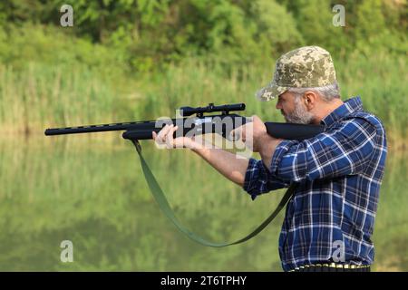 Mann, der mit Jagdgewehr in der Nähe des Sees im Freien zielt Stockfoto