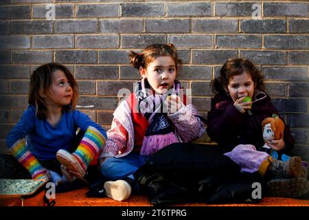 Drei kleine Kinder bei einem Frauenfußballspiel in Dulwich Hamlet saßen auf dem Boden und aßen bei einem Snack Stockfoto