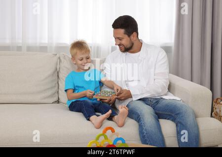 Motorische Entwicklung. Glücklicher Vater hilft seinem Sohn, mit Geoboard und Gummibändern zu Hause auf dem Sofa zu spielen Stockfoto