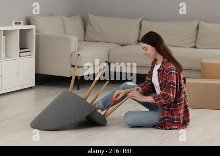 Junge Frau mit Schraubenzieher, die zu Hause einen Sessel auf dem Boden zusammensetzt Stockfoto