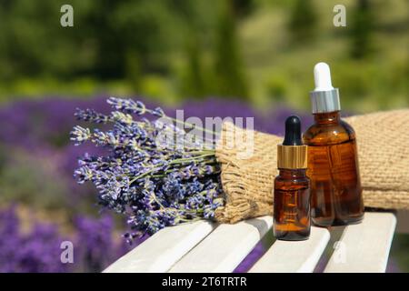 Flaschen mit ätherischem Öl und Lavendelblüten auf weißer Holzoberfläche im Freien, Platz für Text Stockfoto