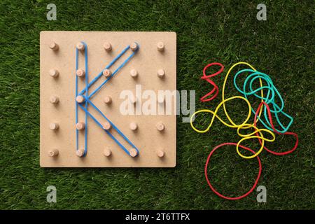 Geoboard aus Holz mit dem Buchstaben K aus Gummibändern auf Kunstrasen, flach gelegt. Lernspielzeug für die motorische Entwicklung Stockfoto