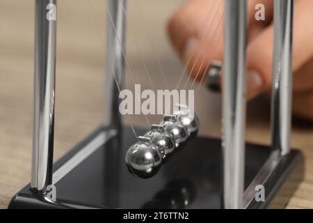 Mann, der mit Newtons Wiege am Tisch spielt, Nahaufnahme. Physikalisches Gesetz der Energieeinsparung Stockfoto