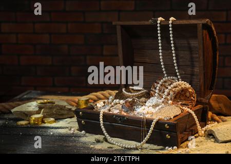 Kiste mit Schätzen und verstreutem Sand auf Holzboden, Platz für Text Stockfoto