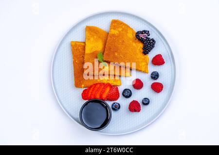 Eine Auswahl an frischen und Reifen Früchten und Beeren auf einem Teller mit einem schwarzen Löffel daneben angeordnet Stockfoto