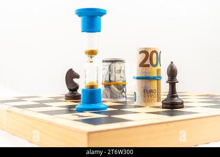 Schachbrett mit schwarzem Bischof und schwarzem Ritter, gerollten Euro- und Dollar-Banknoten und einer Sanduhr. Konzept der Geschäftsstrategie, Führung. Hoch qua Stockfoto