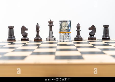 Schachbrett mit einer Reihe schwarzer Figuren, amerikanische Banknoten, die anstelle des schwarzen Königs gerollt und platziert wurden, zwei schwarze Türme, Ritter, Bischöfe, ein schwarzes Qu Stockfoto