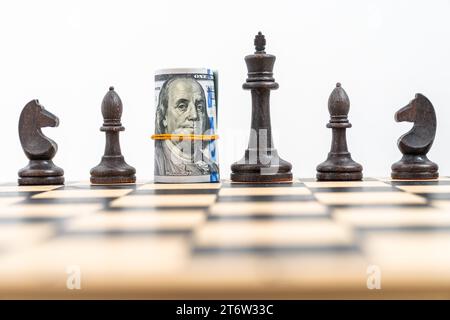 Nahaufnahme des Schachbretts mit einer Reihe schwarzer Figuren, US-Dollar gerollt und platziert anstelle der schwarzen Königin. Konzept der Geschäftsstrategie, Stockfoto
