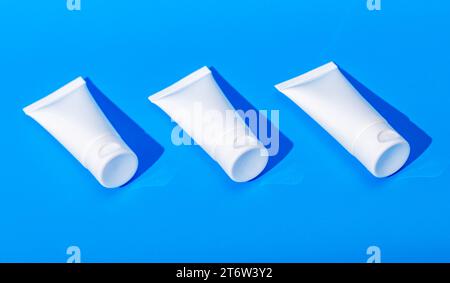 Creme Tubes Mockup Reihe, drei Kosmetikverpackungen, leere weiße Behälter auf blauem Hintergrund Stockfoto