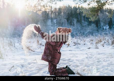 Süßes Mädchen im Wald im Winter wirft Schnee in die Sonnenstrahlen, magisches Licht Stockfoto