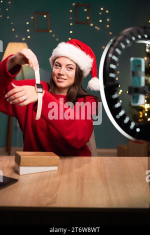 Videowiedergabe. Eine Influencerin zeigt Smart Watch vor der Smartphone-Kamera, legt sie zur Hand, schreibt Inhalte für ihren Fashion-Blog, sitzend Stockfoto