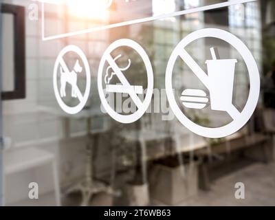 Nahaufnahme: Kein Essen und Trinken, Verbotsschild für Haustiere und Rauchen, weißer Aufkleber an der Glastür des Cafés oder Restaurants. Stockfoto