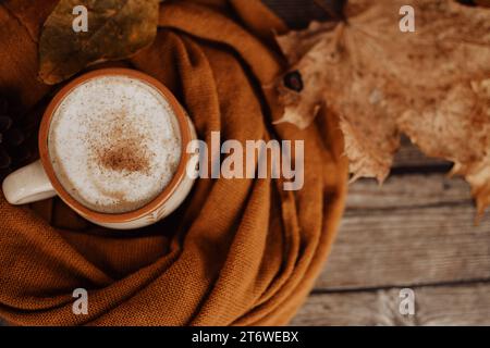 Becher aus Ton, gefüllt mit weißem Kaffee, auf dunklem hölzernem Hintergrund, in warmen und gemütlichen, braunen handgefertigten Schal gewickelt Stockfoto