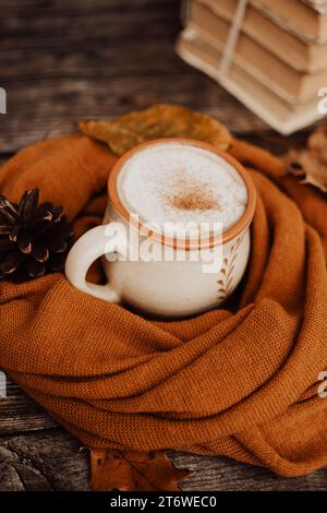 Becher aus Ton, gefüllt mit weißem Kaffee, auf dunklem hölzernem Hintergrund, in warmen und gemütlichen, braunen handgefertigten Schal gewickelt Stockfoto