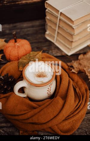 Becher aus Ton, gefüllt mit weißem Kaffee, auf dunklem hölzernem Hintergrund, in warmen und gemütlichen, braunen handgefertigten Schal gewickelt Stockfoto